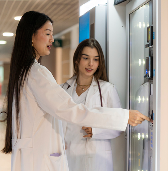 Two young doctors in white coats choosing snacks from a vending machine during a break